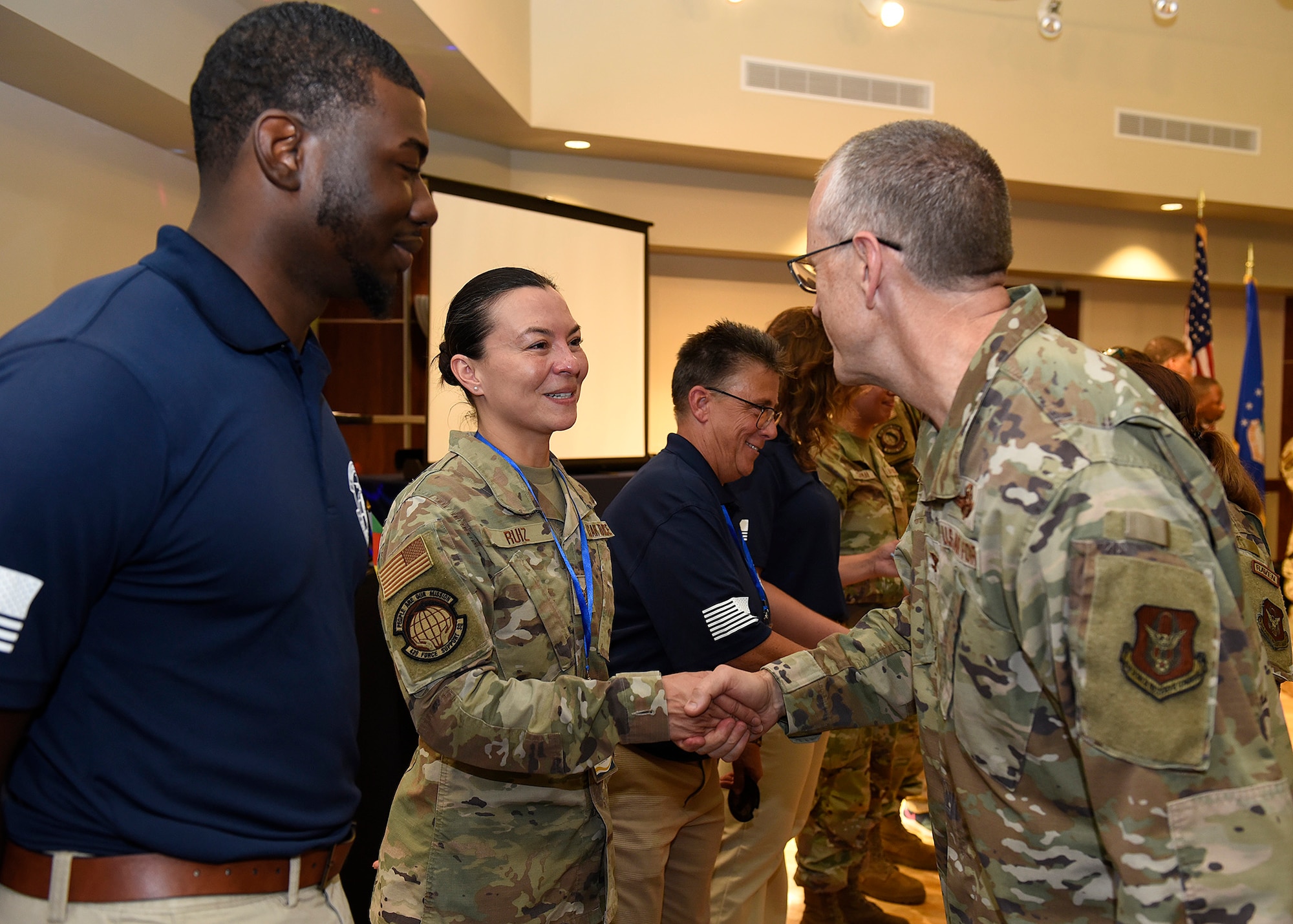 Technical Sgt. Lina Ruiz, 439th Force Support Squadron’s Military Personnel section is presented a challenge coin for her efforts during the Innovation Day from Col Greg Buchanan, 439th Airlift Wing Commander, Sep. 6.  She and Colonel Buchanan are wearing desert camouflage uniforms.  Standing on either side of Ruiz are people wearing blue polo shirts and tan pants.  In the background is a white projection screen.