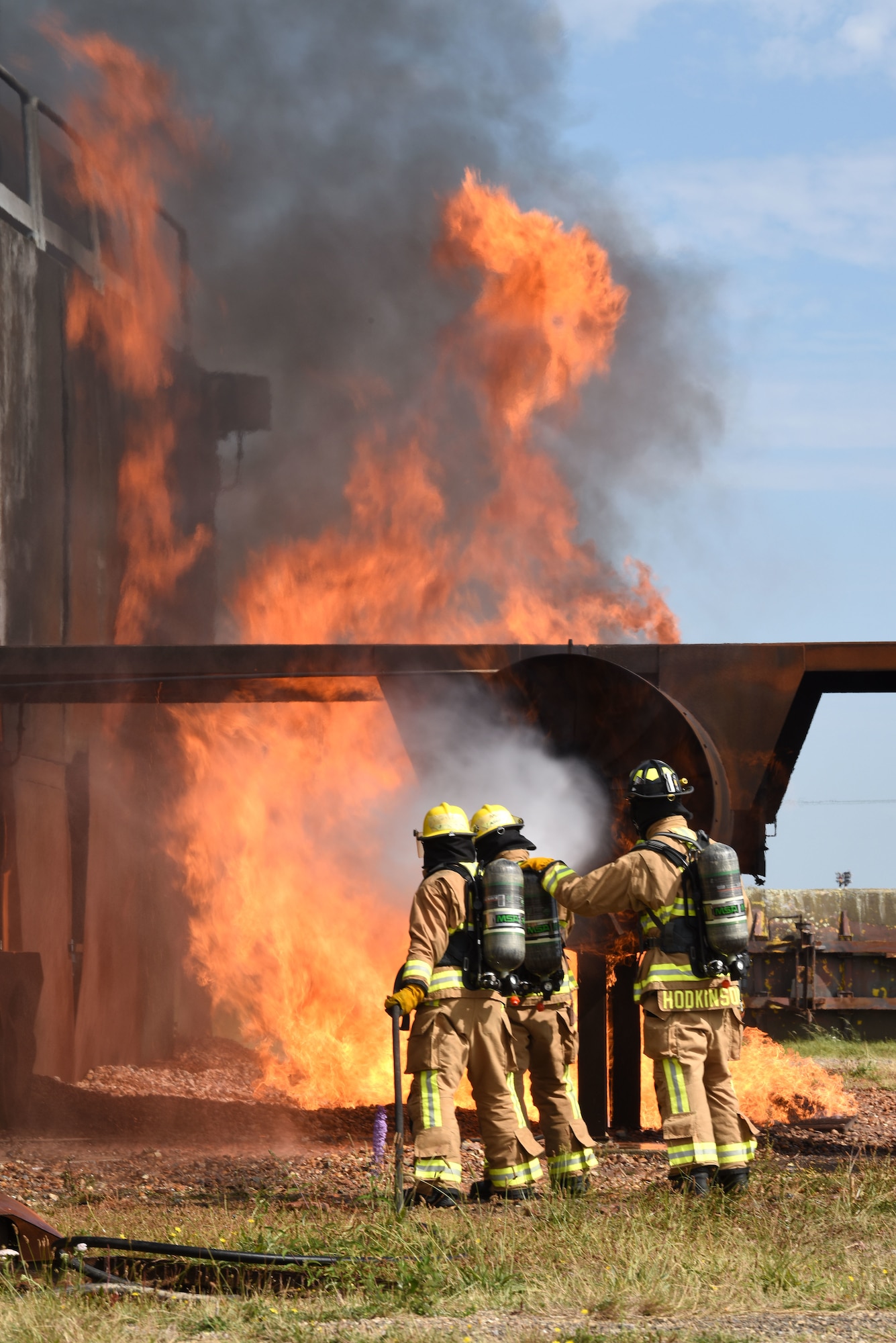 U.S. Air Force Airman Corban La Quey, left, and Airman Jeniel DeJesus, center, 100th Civil Engineer Squadron Fire Department firefighter rookies, spray water onto flames on a mock aircraft live fire trainer, backed up by Daniel Hodkinson, 100th CES Fire Department British civilian firefighter, at the end of their “Rookie Academy” at Royal Air Force Mildenhall, England, Aug. 28, 2024. The Rookie Academy is an intense training program put together by the RAF Mildenhall Fire Department, condensing four months of training for new firefighters into three weeks. (U.S. Air Force photo by Karen Abeyasekere)