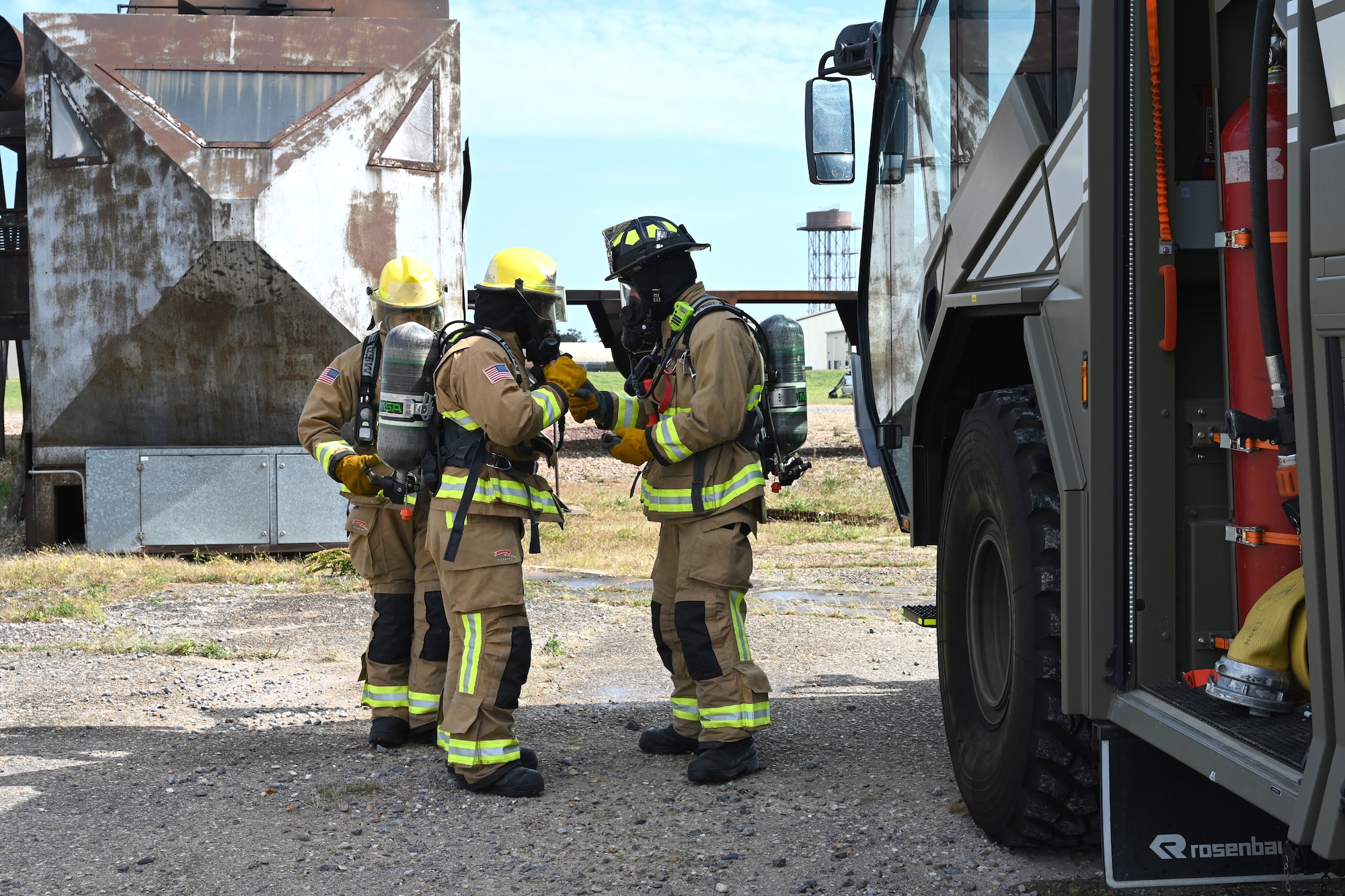 U.S. Air Force Airman Corban La Quey, left, and Airman Jeniel DeJesus, center, 100th Civil Engineer Squadron Fire Department firefighter rookies, get their breathing apparatus checked over and given final safety instructions by Daniel Hodkinson, 100th CES Fire Department British civilian firefighter, before practicing at the live fire trainer at the end of their “Rookie Academy” at Royal Air Force Mildenhall, England, Aug. 28, 2024. The Rookie Academy is an intense training program put together by Staff Sgt. Connor Nance, 100th CES Fire Department assistant chief of training, condensing four months of training for new firefighters into three weeks. (U.S. Air Force photo by Karen Abeyasekere)