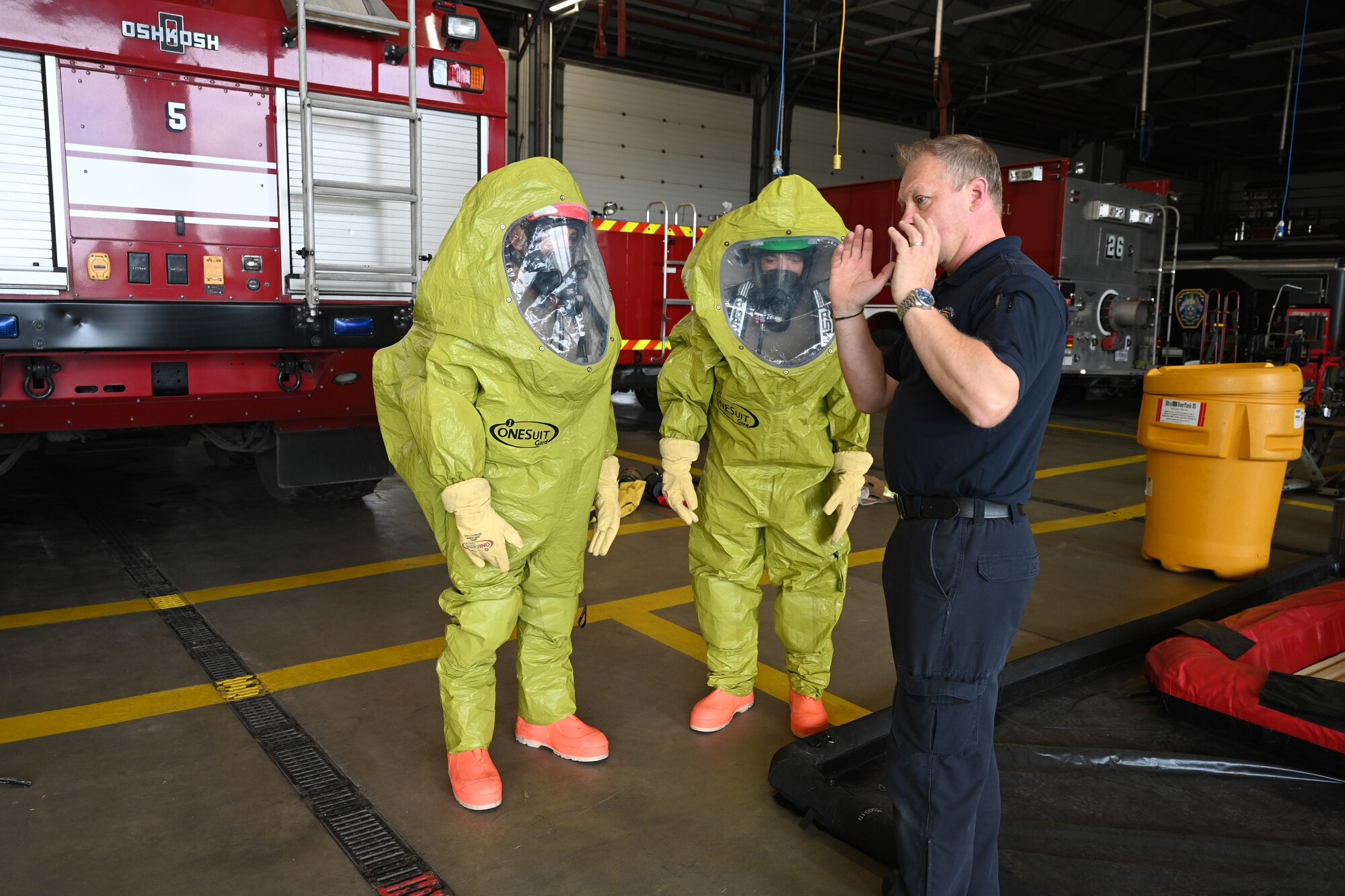 Colin Smith, right, 100th Civil Engineer Squadron Fire Department British civilian firefighter, instructs rookie firefighters on how to safely respond to a hazardous materials incident while wearing decontamination suits as part of “Rookie Academy” training at Royal Air Force Mildenhall, England, Aug. 27, 2024. As part of the program, new rookie firefighters are trained together by different instructors within the fire department, so they learn equipment use and life-saving techniques the same way, rather than being split with different trainers. (U.S. Air Force photo by Karen Abeyasekere)