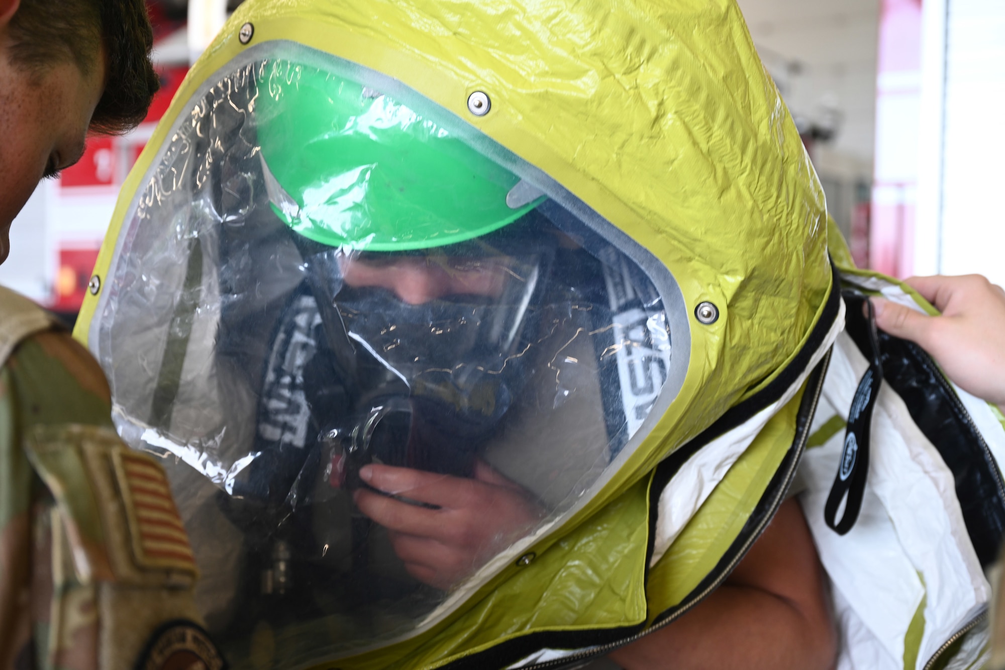 U.S. Air Force Airman 1st Class Jeremiah Crawley, 100th Civil Engineer Squadron Fire Department firefighter rookie, gets helped into his decontamination training suit by fellow firefighters as part of the new “Rookie Academy” program at Royal Air Force Mildenhall, England, Aug. 27, 2024. The Rookie Academy is an intense training program where new rookie firefighters are trained together by different instructors within the fire department, so they learn equipment use and life-saving techniques the same way, rather than being split with different trainers. (U.S. Air Force photo by Karen Abeyasekere)