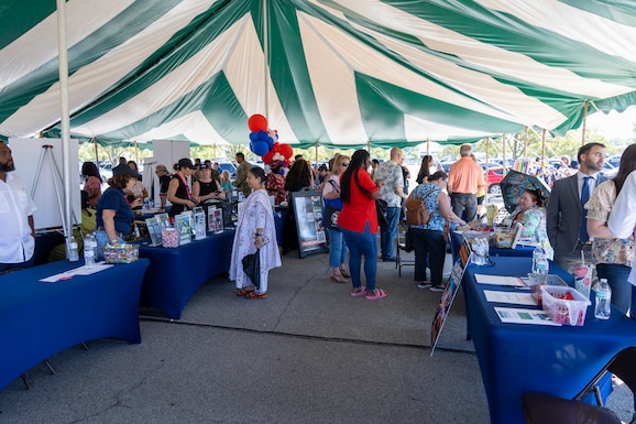 People standing under a green and white tent with blue tables.