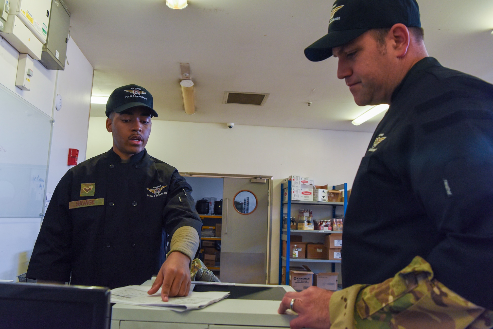 U.S. Air Force Senior Airman Jurell Savage, left, 100th Force Support Squadron Gateway Dining Facility storeroom manager, explains how he plans, tracks, and orders food items to keep the dining facility stocked to Col. Joseph Wall, 100th Air Refueling Wing deputy commander, during a “Day in the Life” immersion at Royal Air Force Mildenhall, England, Sept. 13, 2024.