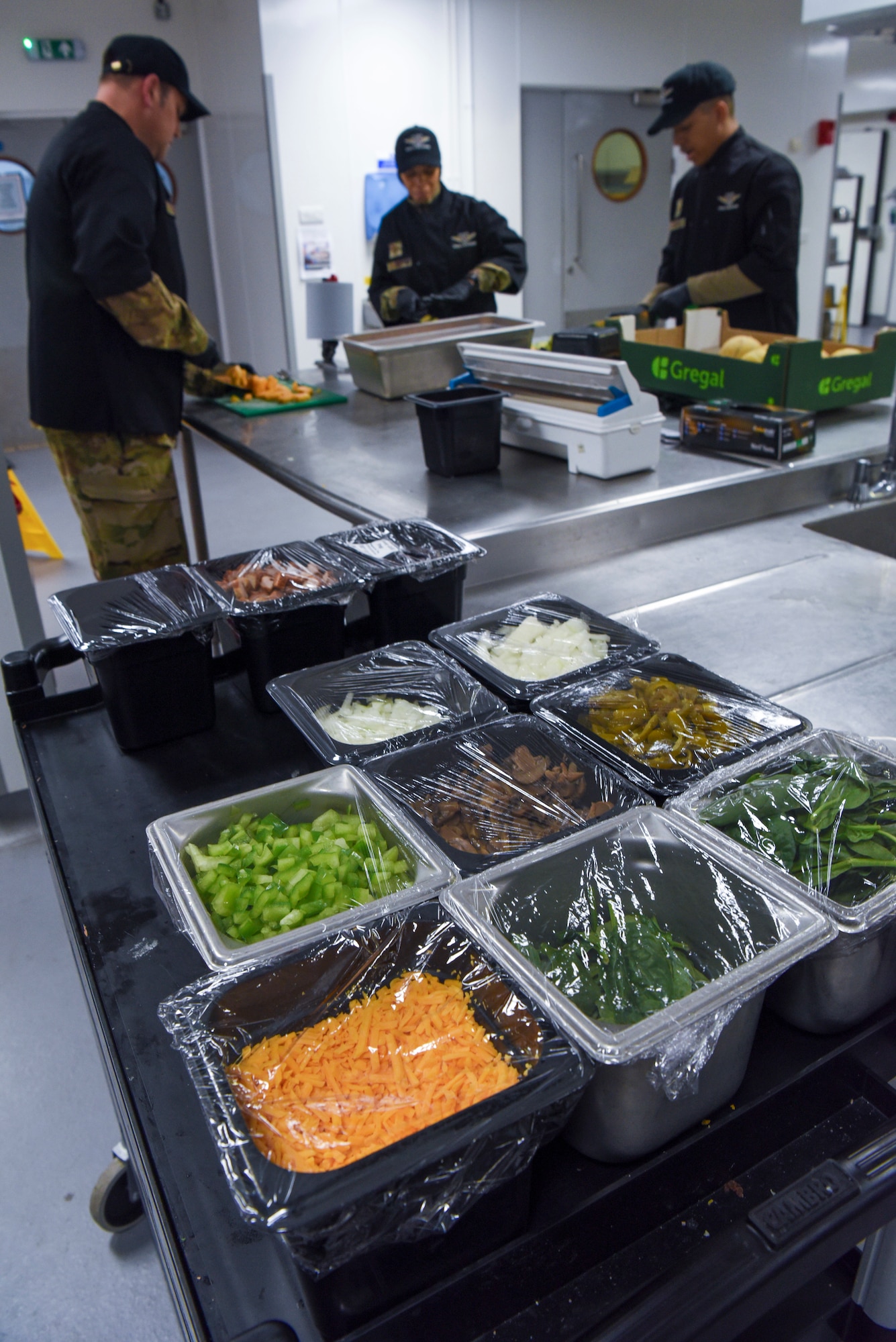 U.S. Air Force Col. Joseph Wall, left, 100th Air Refueling Wing deputy commander, and Chief Master Tiffany Griego, center, 100th ARW command chief, cut cantaloupe in preparation for a meal alongside Senior Airman Jurell Savage, 100th Force Support Squadron Gateway Dining Facility storeroom manager, during a “Day in the Life” immersion at Royal Air Force Mildenhall, England, Sept. 13, 2024.