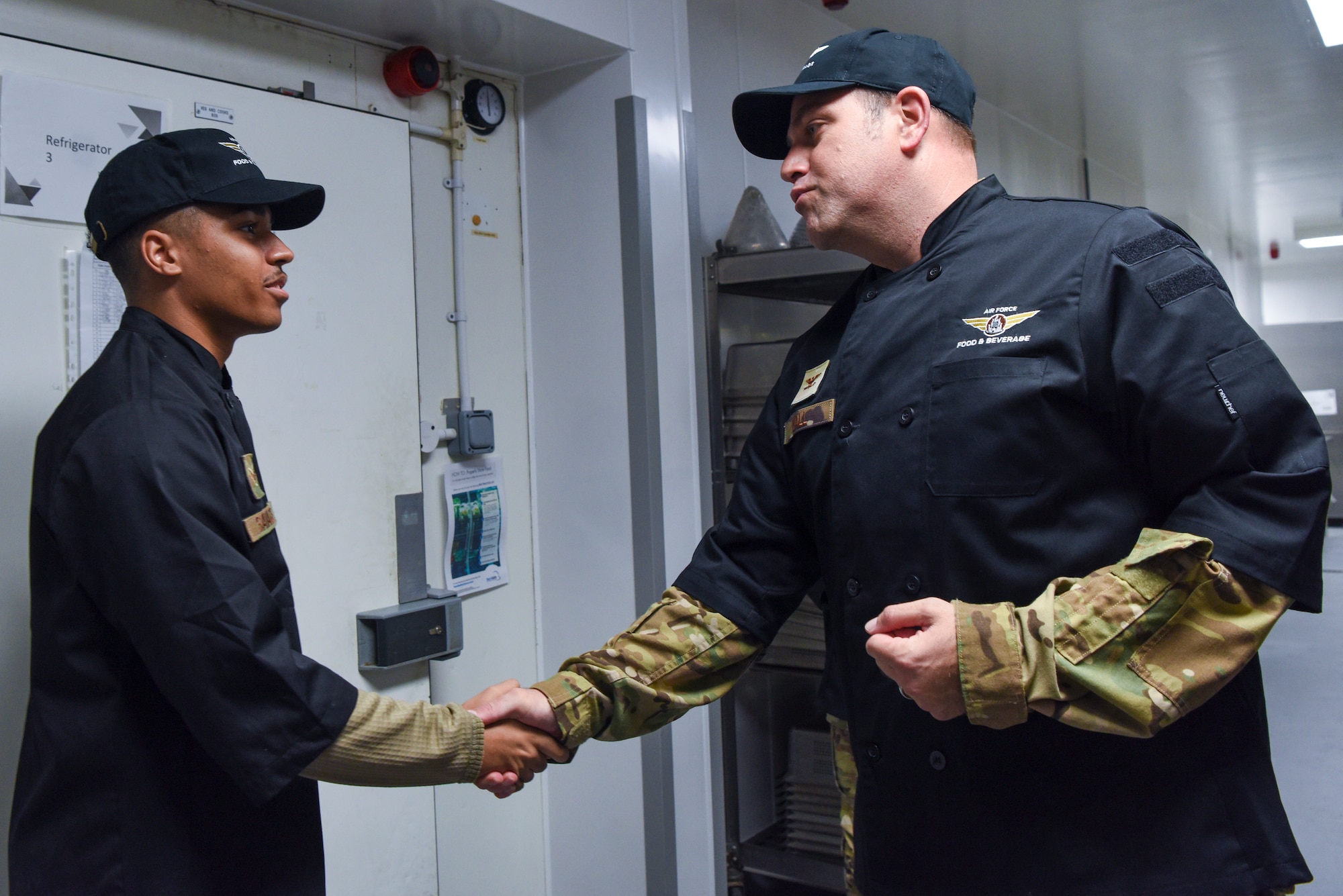 U.S. Air Force Col. Joseph Wall, right, 100th Air Refueling Wing deputy commander, coins Senior Airman Jurell Savage, 100th Force Support Squadron Gateway Dining Facility storeroom manager, during a “Day in the Life” immersion with the 100th Force Support Squadron Gateway Dining Facility at Royal Air Force Mildenhall, England, Sept. 13, 2024.