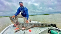 Man poses with a dead alligator on the bow of a boat