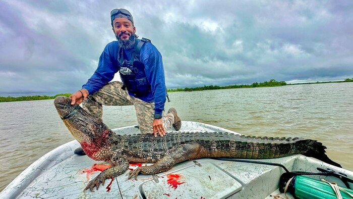 Man poses with a dead alligator on the bow of a boat