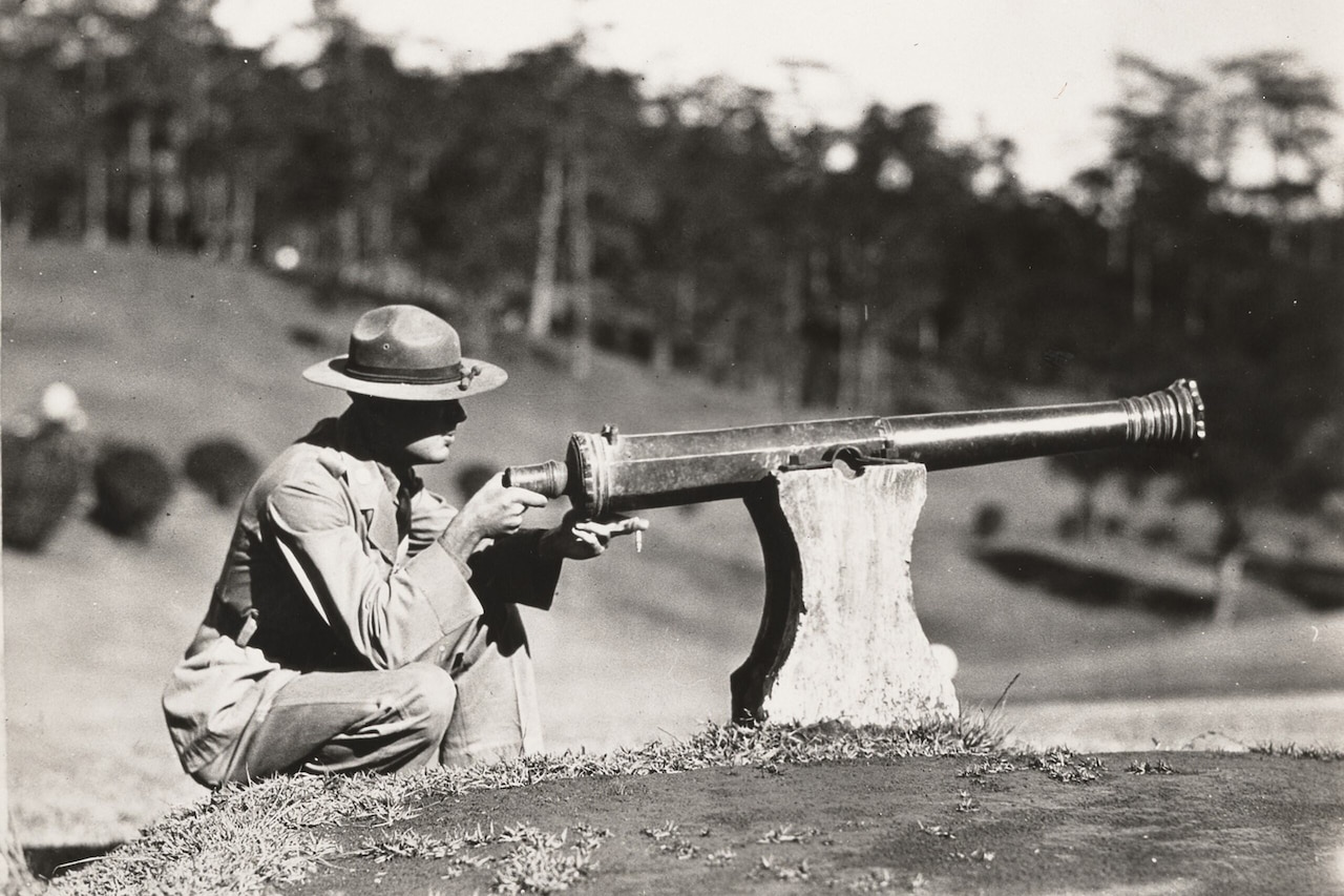 A soldier looks at the blunt end of a small cannon.
