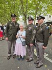 Maj. Gen. John Rueger, 35th Infantry Division commander, Command Sgt. Maj. Rob Istas, and Aide-de Camp Maj. Dustin Dice with a resident in Orleans, France, Aug. 16, 2024. The command team visited France for the 80th anniversary of the liberation of Orleans. The woman is holding a photo of herself as an 8-year-old girl, posing with the 35th Infantry Division Soldiers who liberated her city on Aug. 16, 1944.
