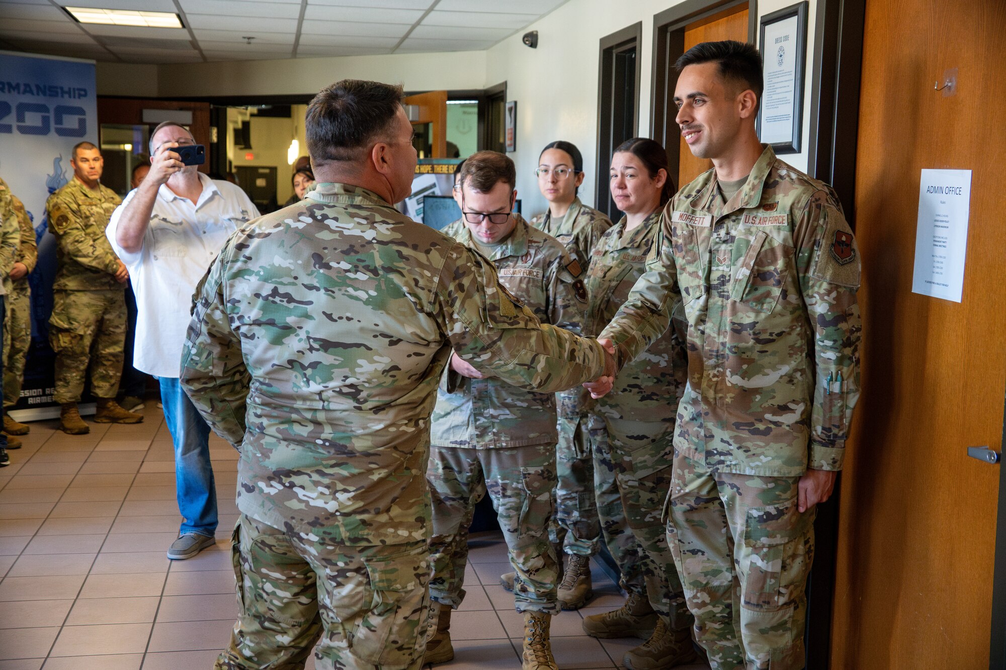 An Airman shakes another Airman's hand while people look on.