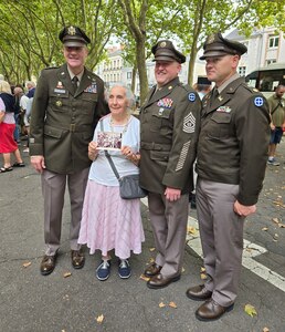 Maj. Gen. John Rueger, 35th Infantry Division commander, Command Sgt. Maj. Rob Istas, and Aide-de Camp Maj. Dustin Dice with a resident in Orleans, France, Aug. 16, 2024, the 80th anniversary of the liberation of Orleans. The woman is holding a photo of herself as an 8-year-old girl, posing with the 35th Infantry Division Soldiers who liberated her city on Aug. 16, 1944.