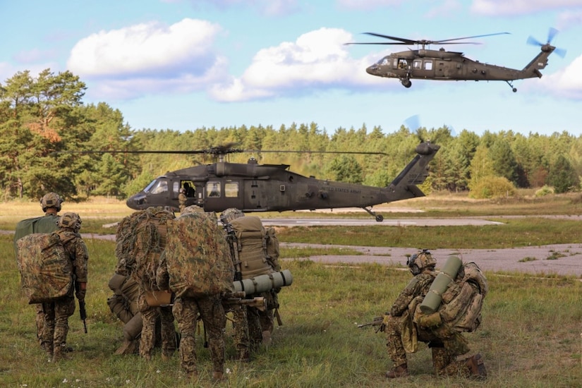 Soldiers train in a field near helicopters.