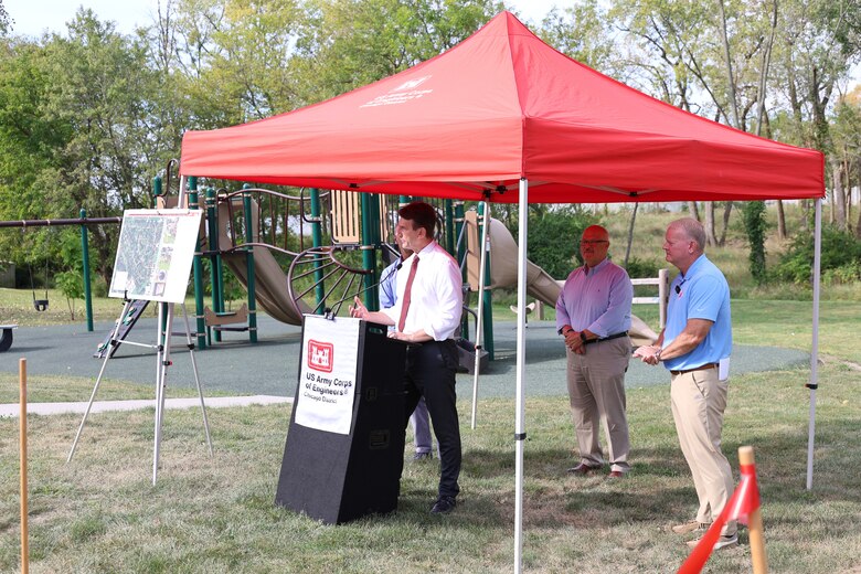 Man stands behind podium under a red canopy to give a speech.