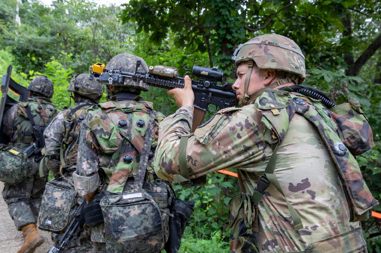 Soldiers with guns walk in file through the woods.