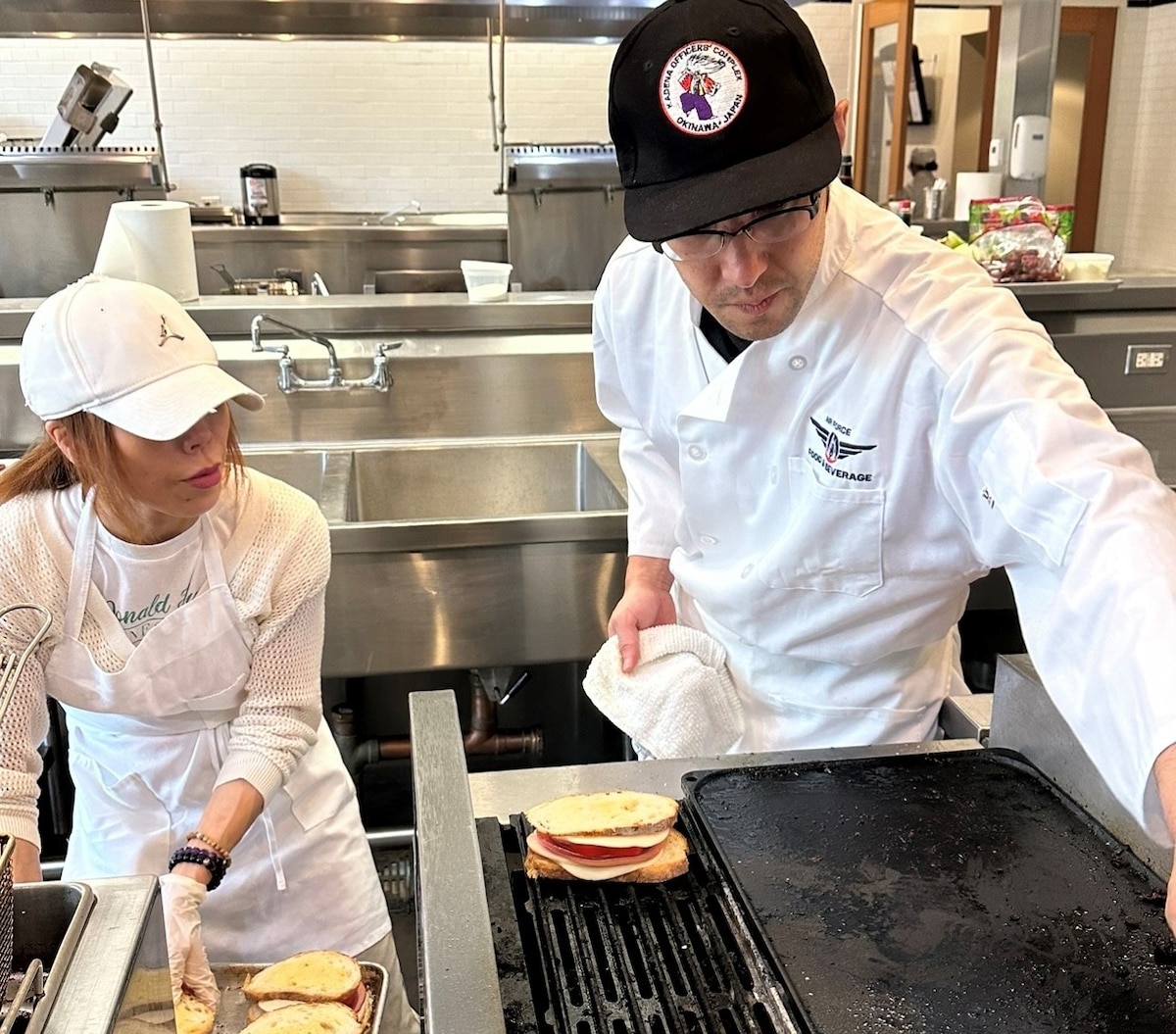One student moves sandwiches near a grill while another places them on the grill