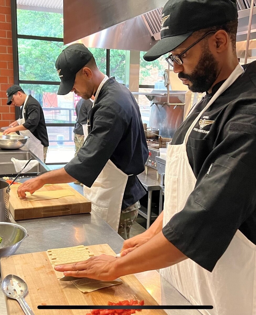 side view of row of three Airmen cutting strips of fresh pasta