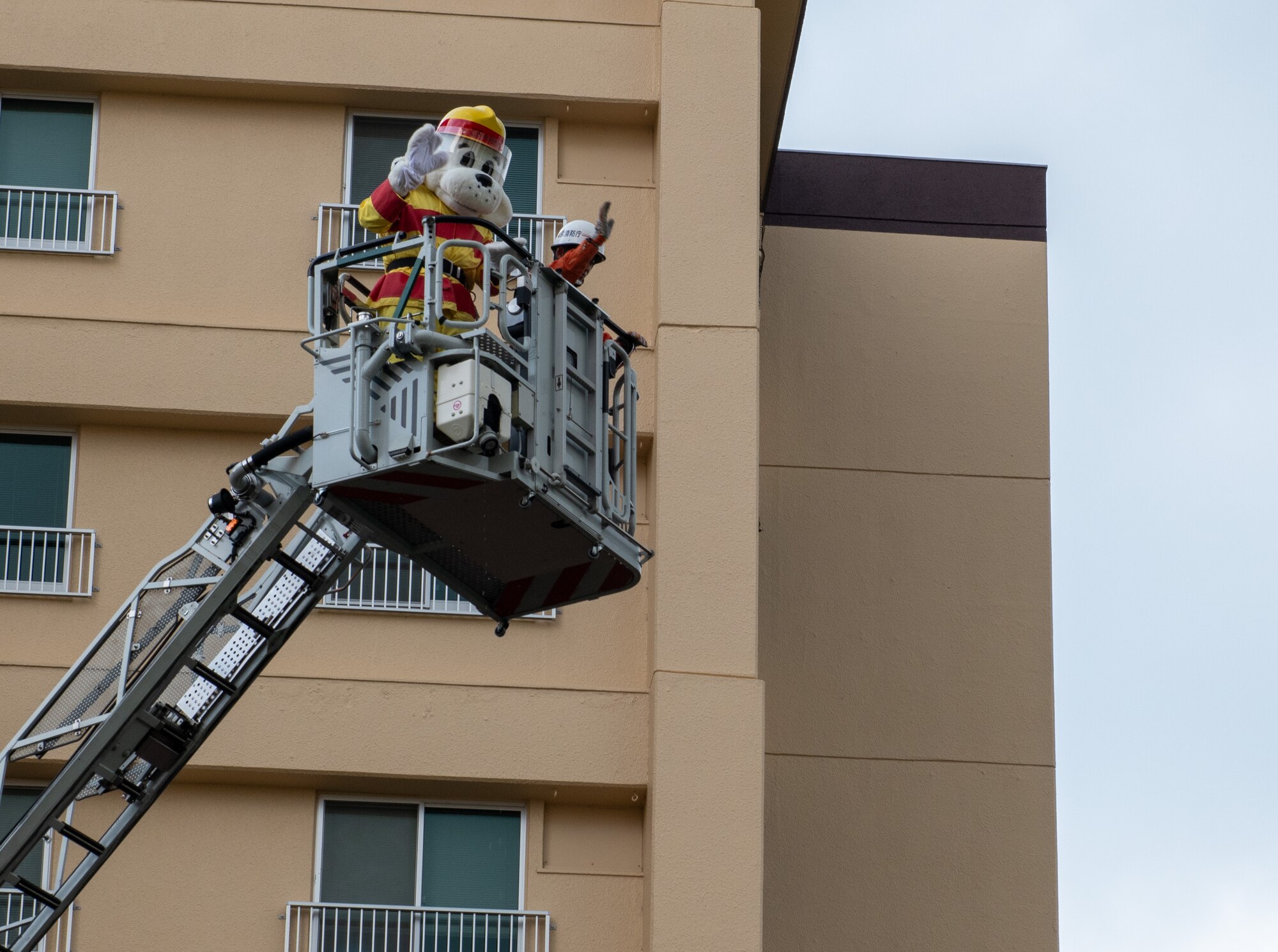 Sparky the Fire Dog and Tokyo Fire Department firefighter wave to a crowd.