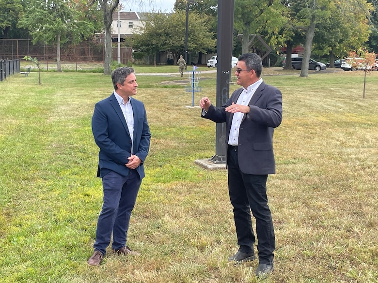 Two individuals discuss a project in a field area adjacent to homes