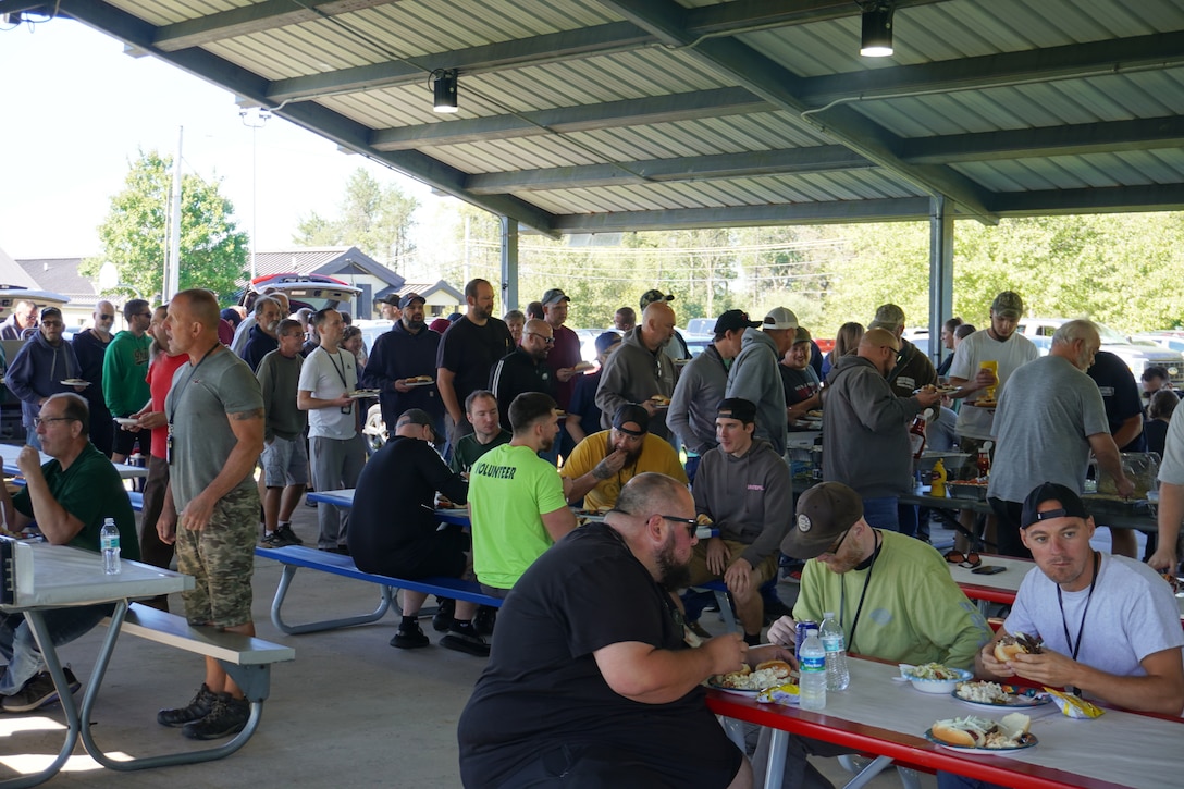A large group of people sit at picnic tables under a canopy.