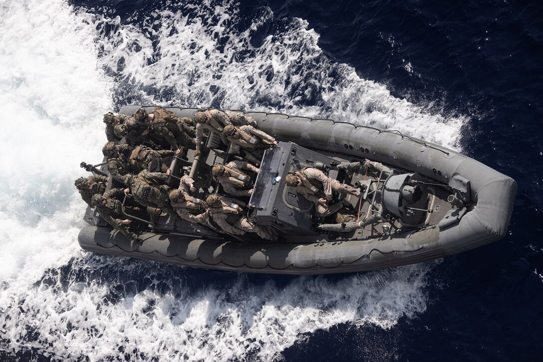 An overhead view of a group of Marines in an inflatable boat in open water during daylight.