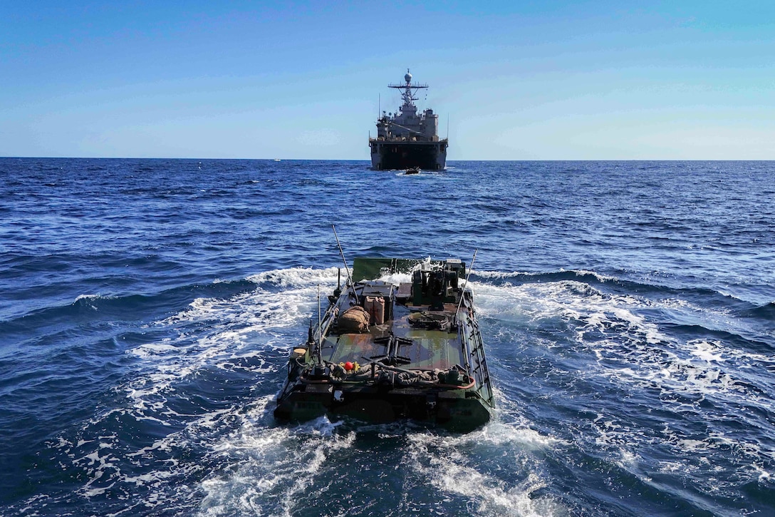 A small combat boat sails behind a ship in a body of water during daylight.