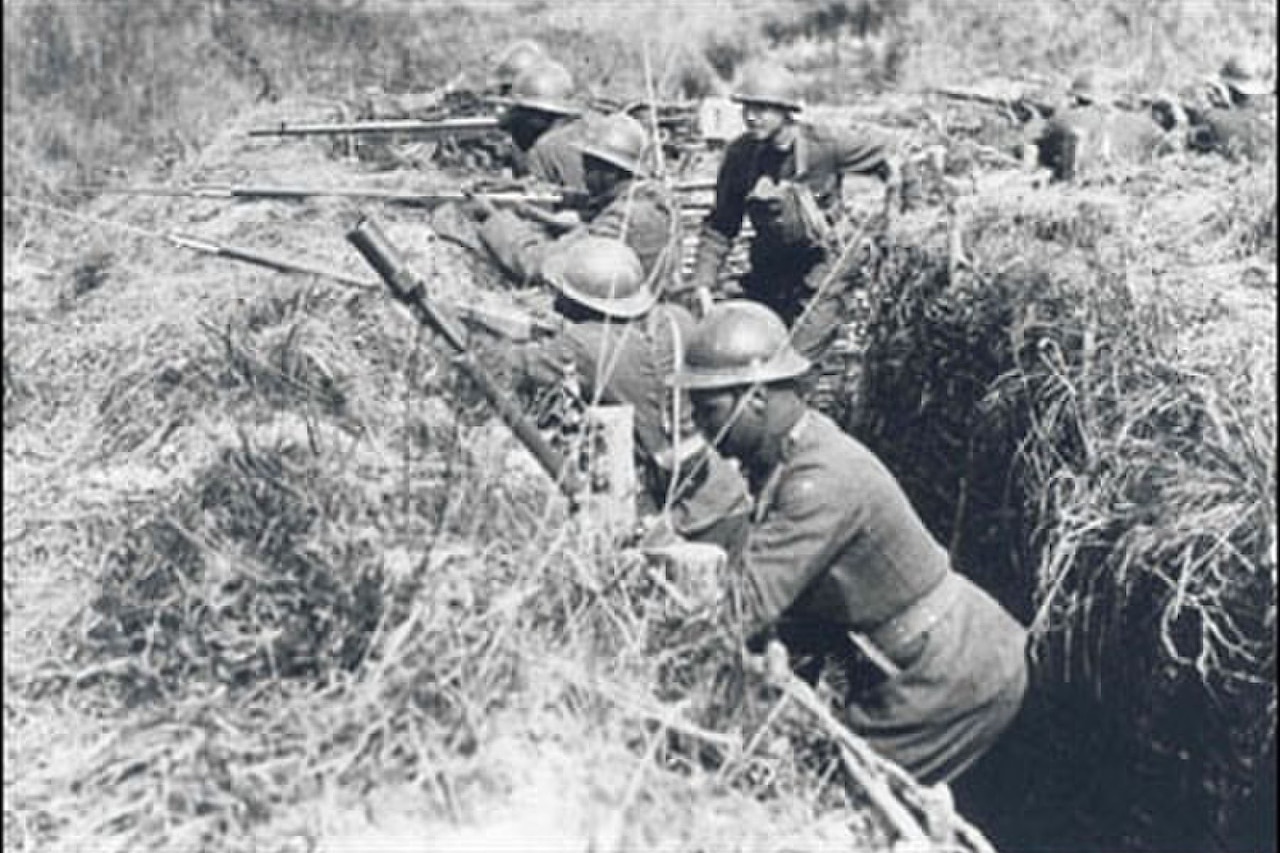 Men practice shooting rifles from a dug-out trench.