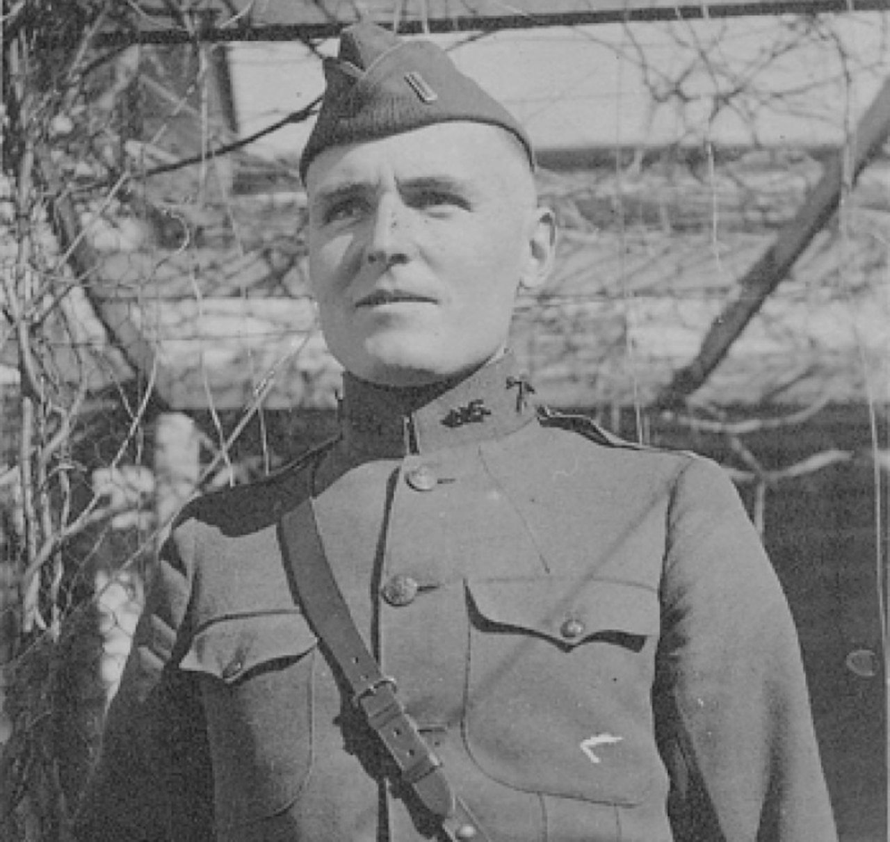 A man wearing a uniform and cap looks into the distance.