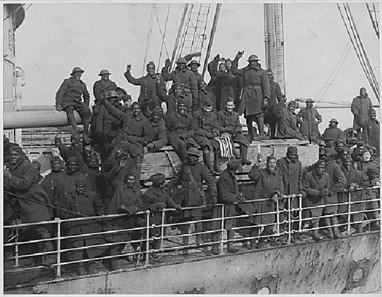 Several men cheer and wave from the side of a large ship.