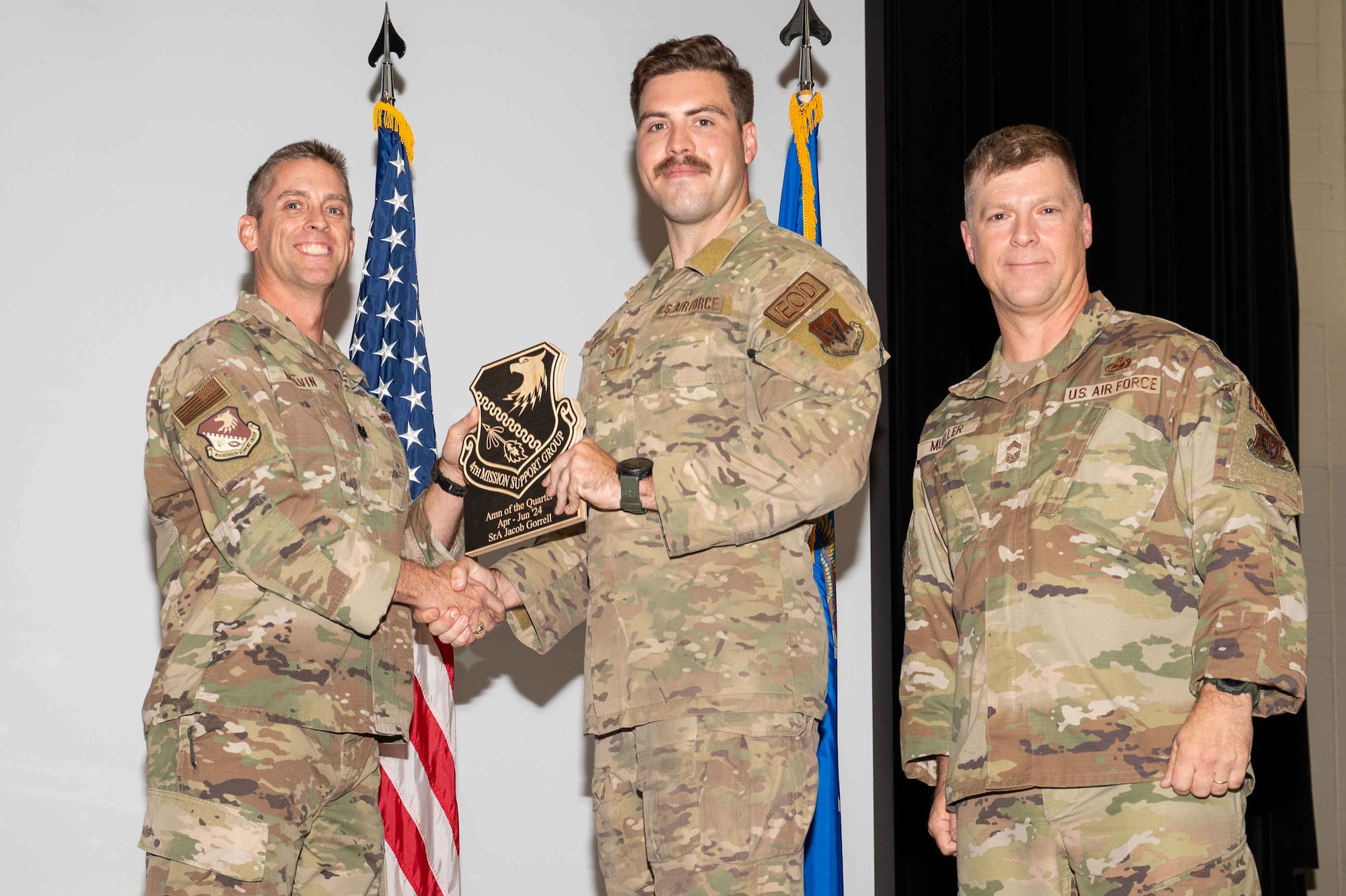 U.S. Air Force Senior Airman Jacob Gorrell, center, 4th Civil Engineer Squadron explosive ordnance disposal team member, accepts the Airman of the 2nd Quarter Award from Col. James Melvin, left, 4th Mission Support Group deputy commander, and Chief Master Sgt.  Edward Mueller, 4 MSG senior enlisted leader, during the 4 MSG 2nd Quarter Awards ceremony at Seymour Johnson Air Force Base, North Carolina, July 26, 2024. Quarterly Awards are awarded to Airmen and civilians in different categories including civilians and Airmen of the quarter. (U.S. Air Force photo by Airman 1st Class Rebecca Tierney)