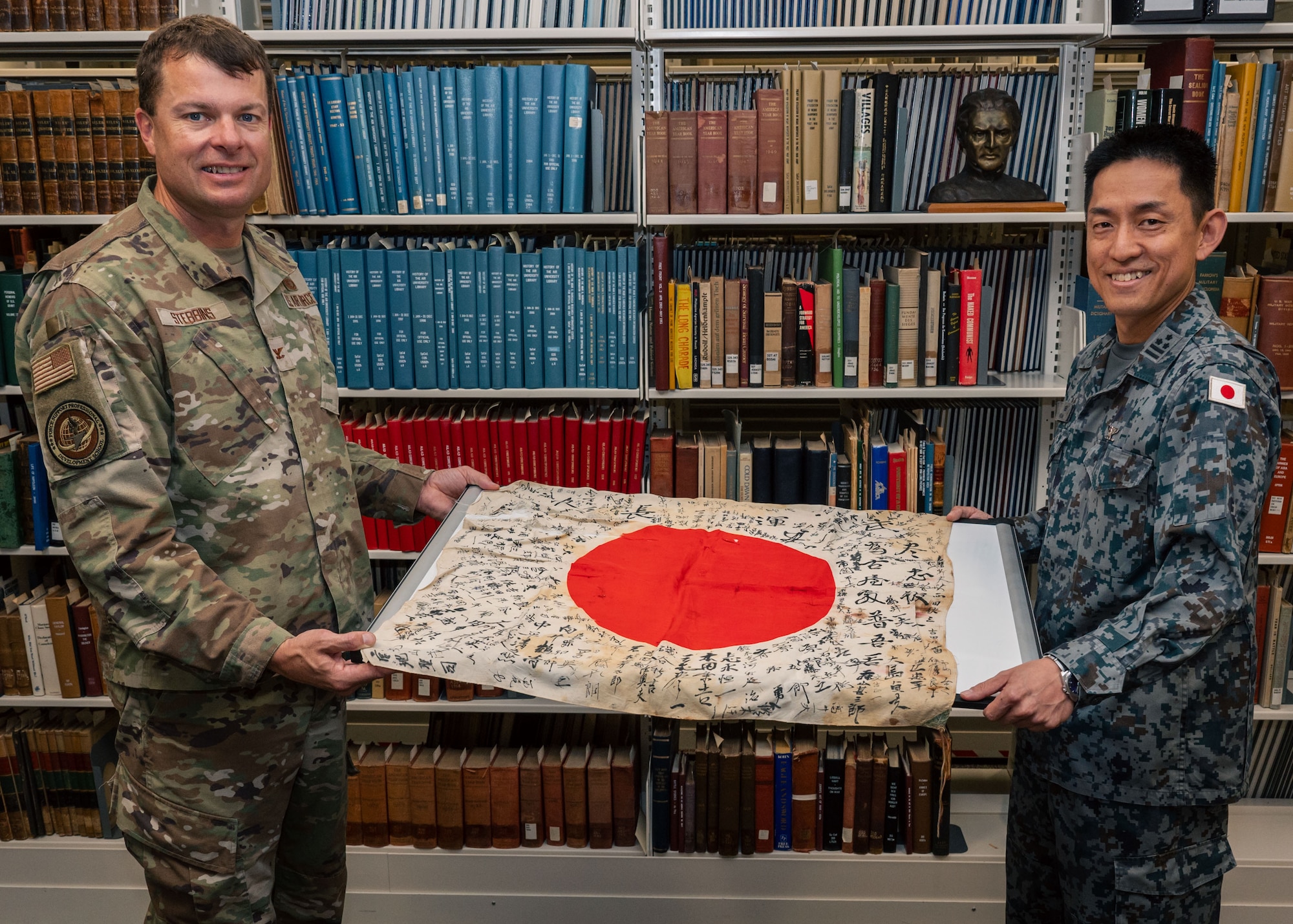 Col. Ryan Stebbins, the 42nd Air Base Wing’s Force Support Professional Development School director, and Japanese Col. Hirokazu Honda, an Air War College student, pose for a photo with a Japanese “Good Luck Flag” at Maxwell Air Force Base, Alabama, Sept. 16, 2024. The Yosegaki Hinomaru (Good Luck Flag) was commonly carried by Japanese soldiers in WWII while going into battle. (U.S. Air Force photo by Senior Airman Evan Lichtenhan)