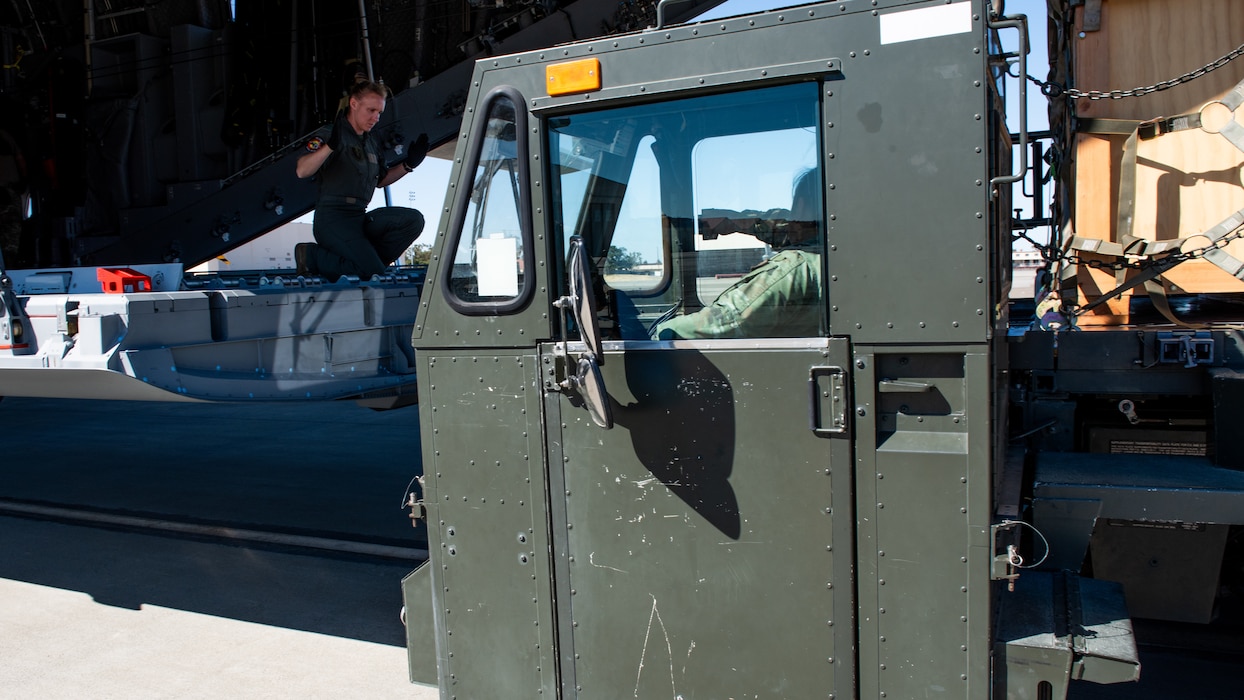 Foreign service member directs loader toward aircraft bay