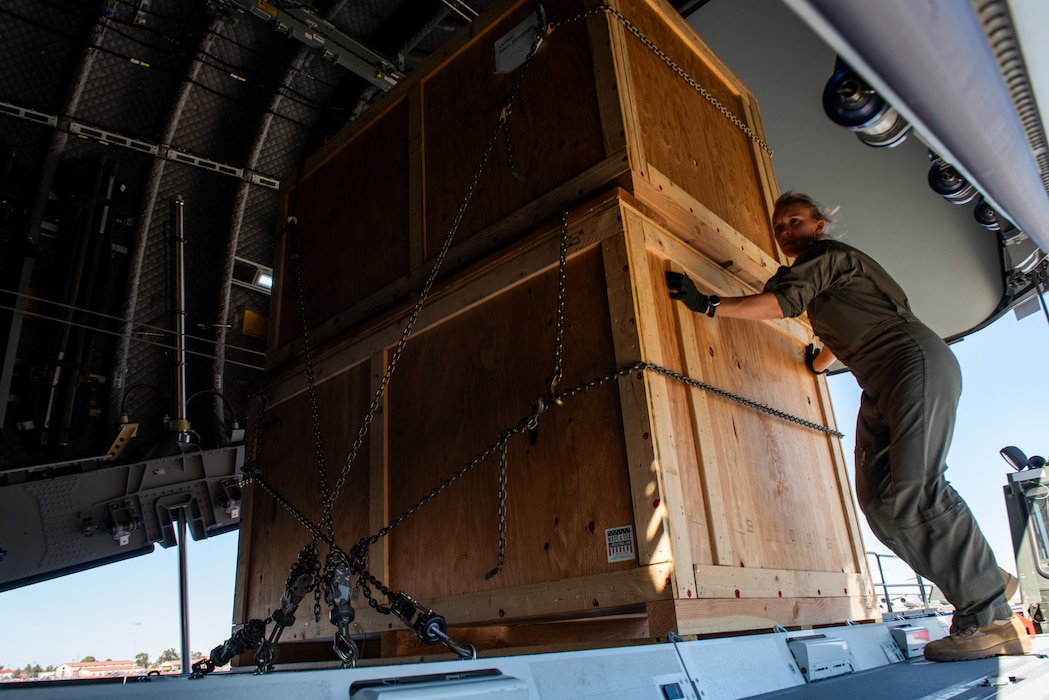 Foreign service member pushing crate into aircraft bay.