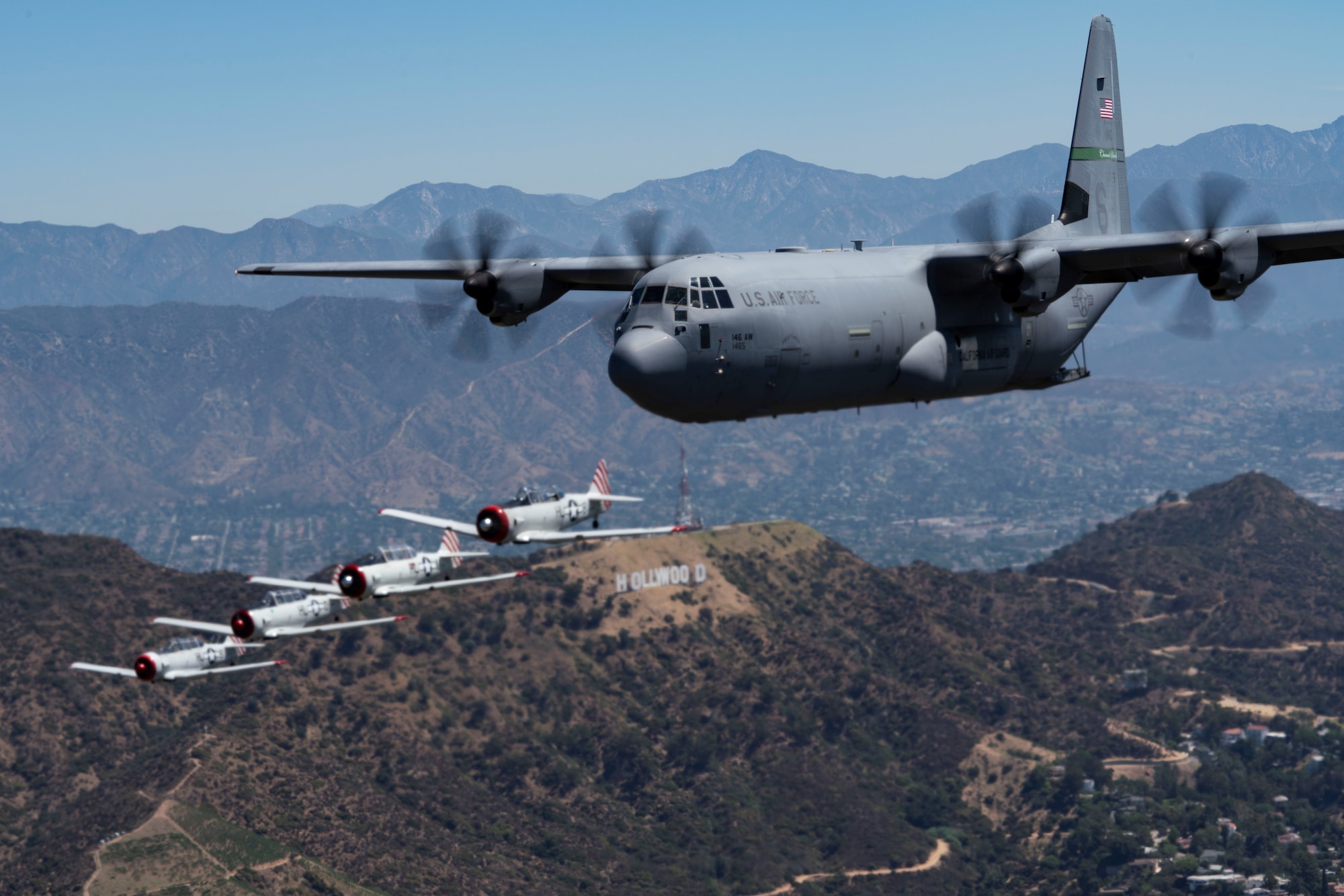 C-130J Super Hercules aircraft fly's above the Hollywood sign in a formation flight with other world war 2 aircraft.