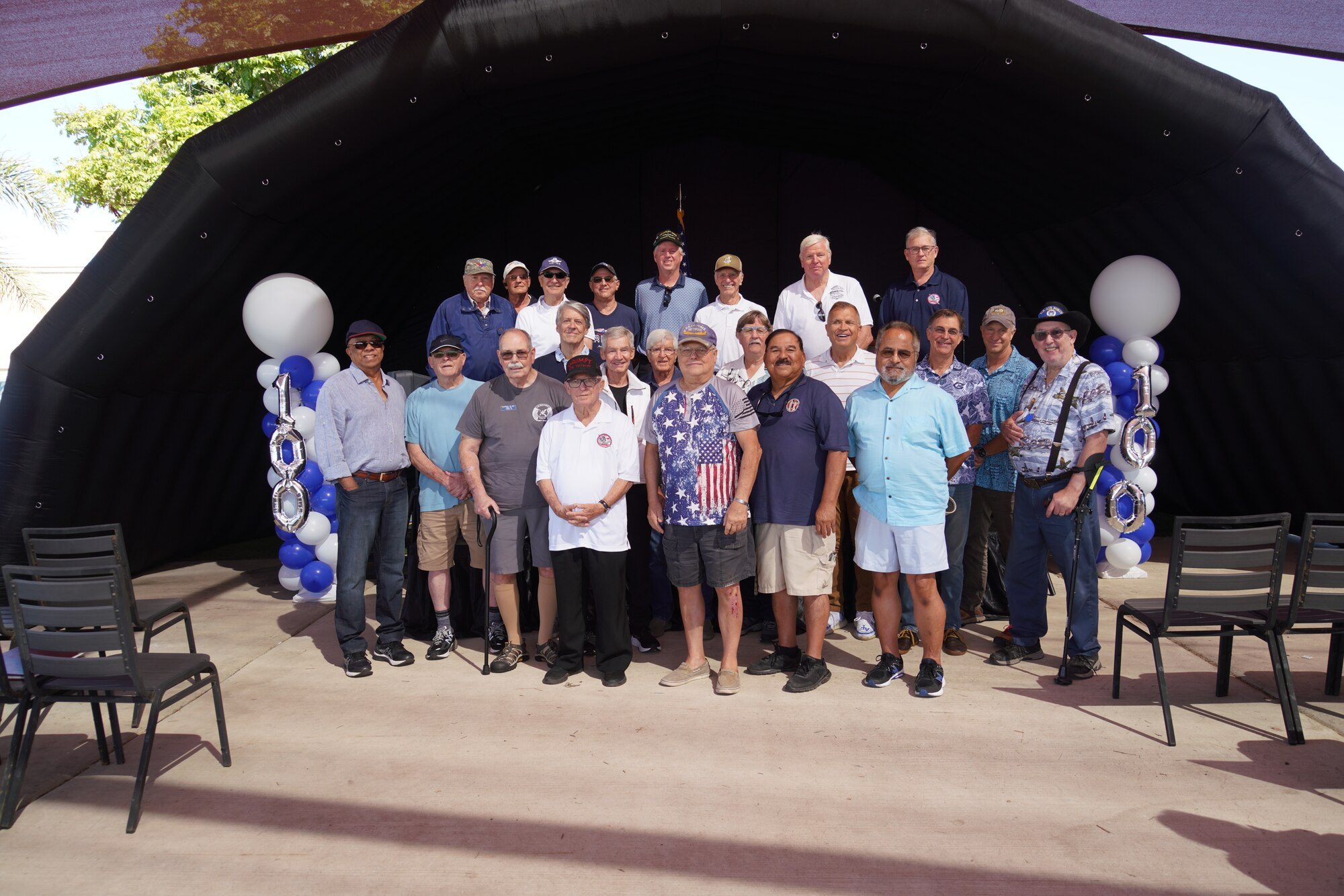 Past members of the 146th Airlift Wing pose for a photo in front of a stage during the centennial celebration of the "Hollywood Guard" at the Channel Islands Air National Guard Station, Port Hueneme, California, Aug. 4, 2024. U.S. Air National Guard photo by Tech. Sgt. Michelle Ulber.