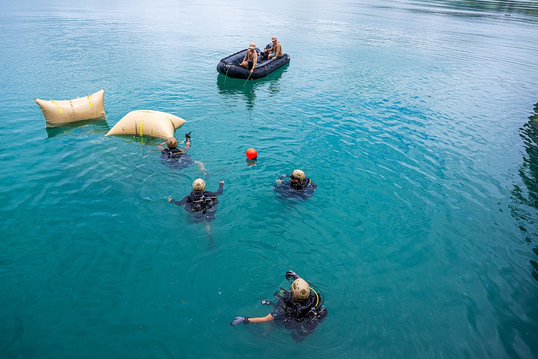 Four U.S. and South Korean sailors swim around buoys in open water as two others operate a raft during a daylight training exercise.