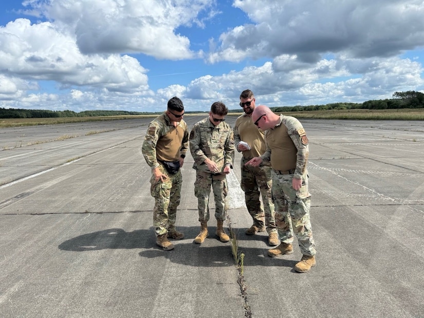 Four airmen work on tarmac under cloudy, blue sky.