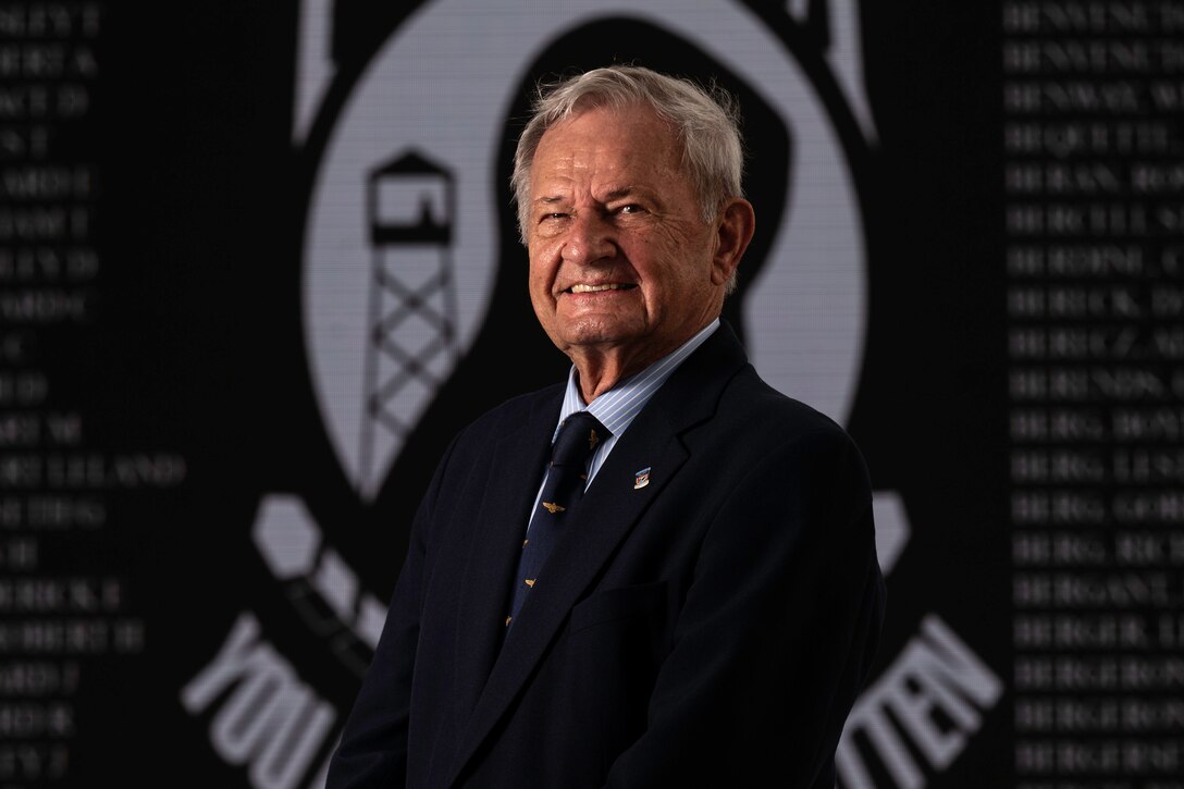 A man poses in front of the prisoner of war flag.