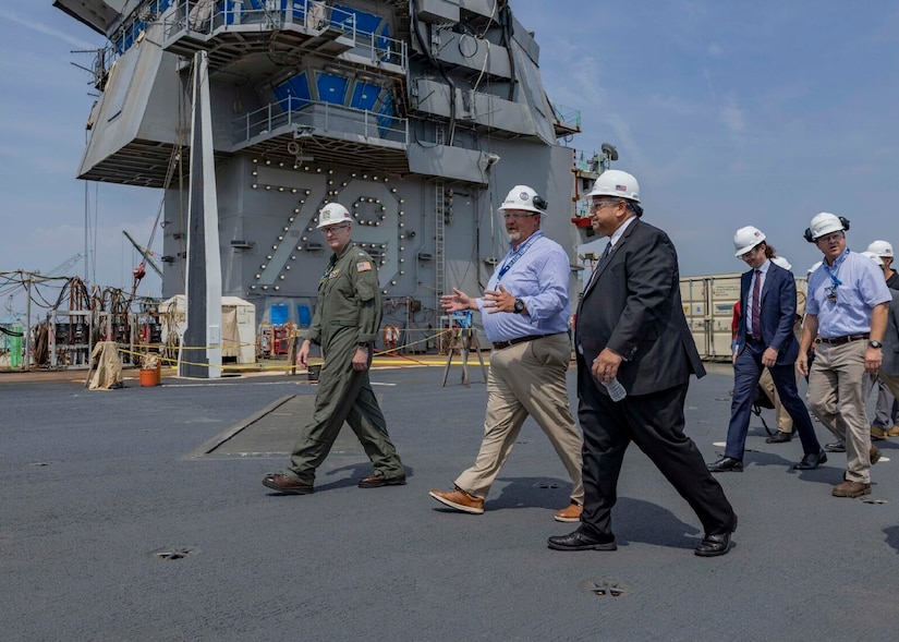 Men walk along the deck of an aircraft carrier under construction.