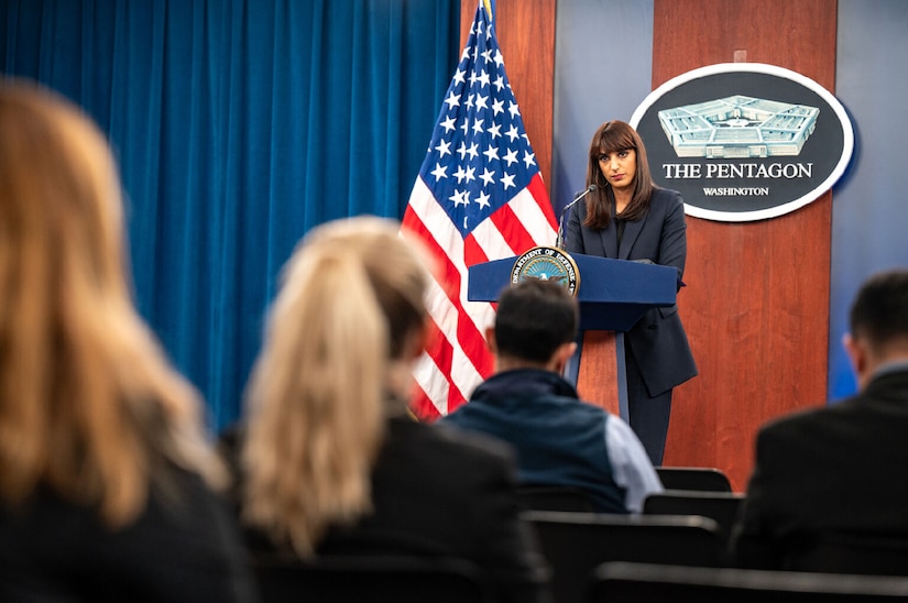 A woman stands a lectern answering questions.