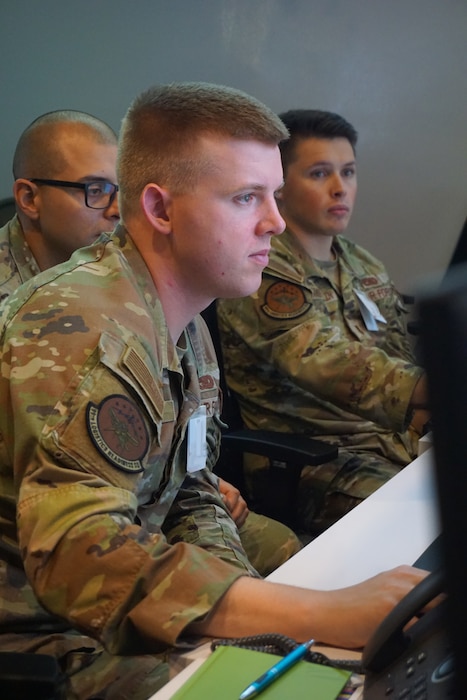 three uniformed U.S. Air Force Airmen work at computers