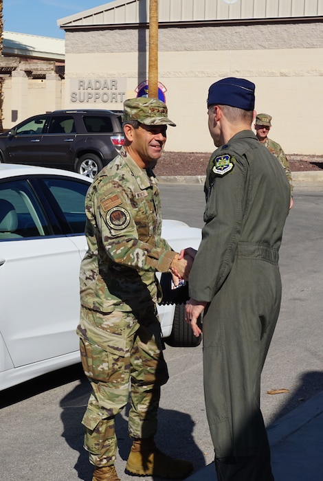 two uniformed U.S. Air Force Airmen shake hands outside in front of a white vehicle