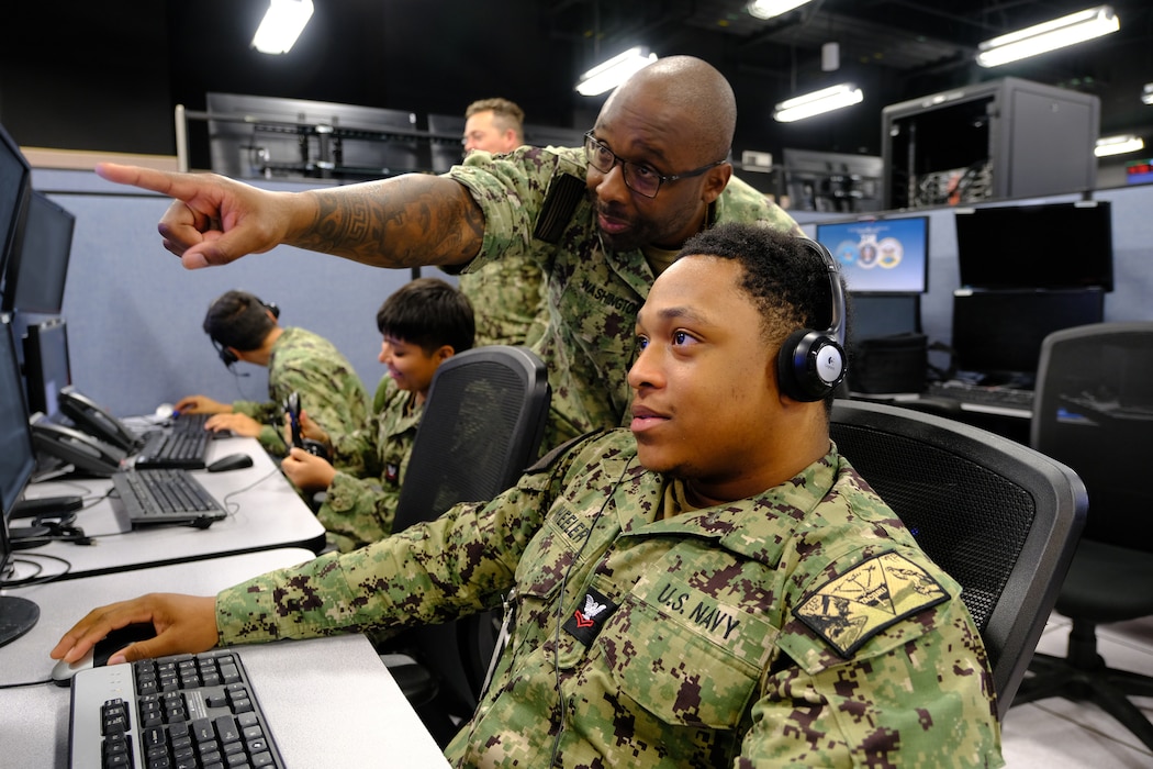 two uniformed U.S. Navy Sailors work at a computer