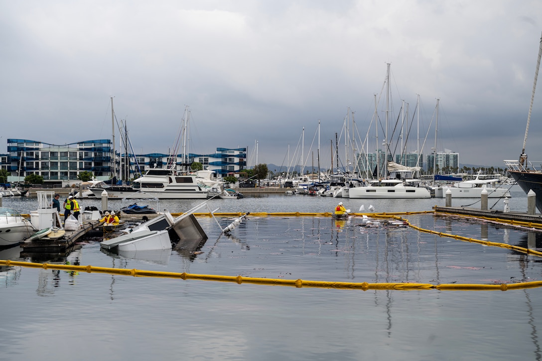 A sunken vessel is seen with boom surrounding it in a marina.