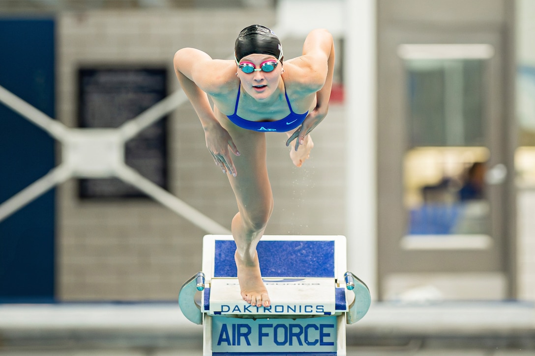 A cadet wearing a swim cap and goggles dives off a diving board.