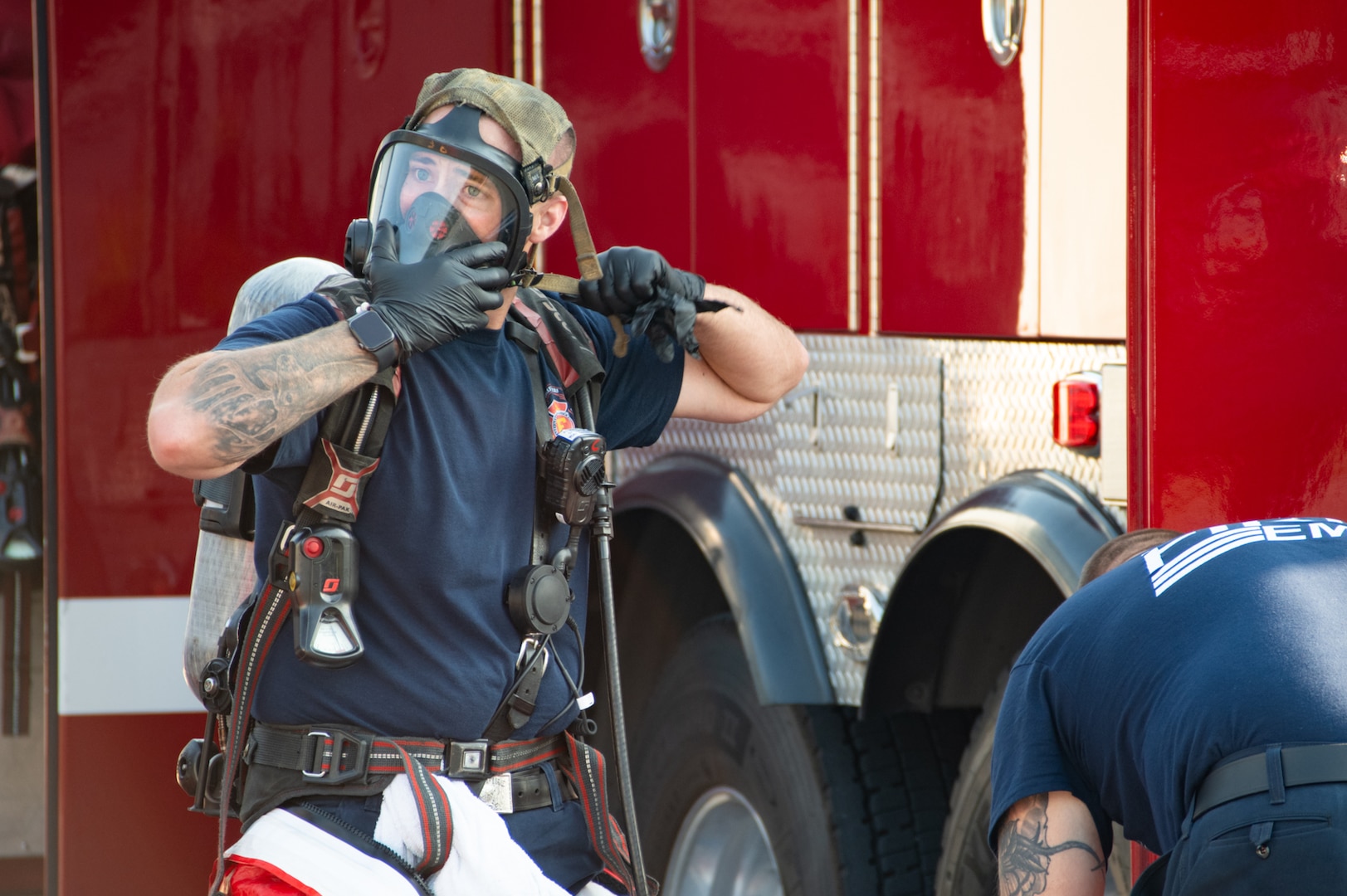 A firefighter puts on a protective mask while standing in front of a firetruck