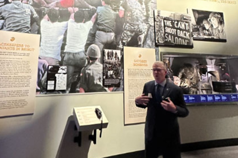 A person in a business suit speaks in front of a diorama.