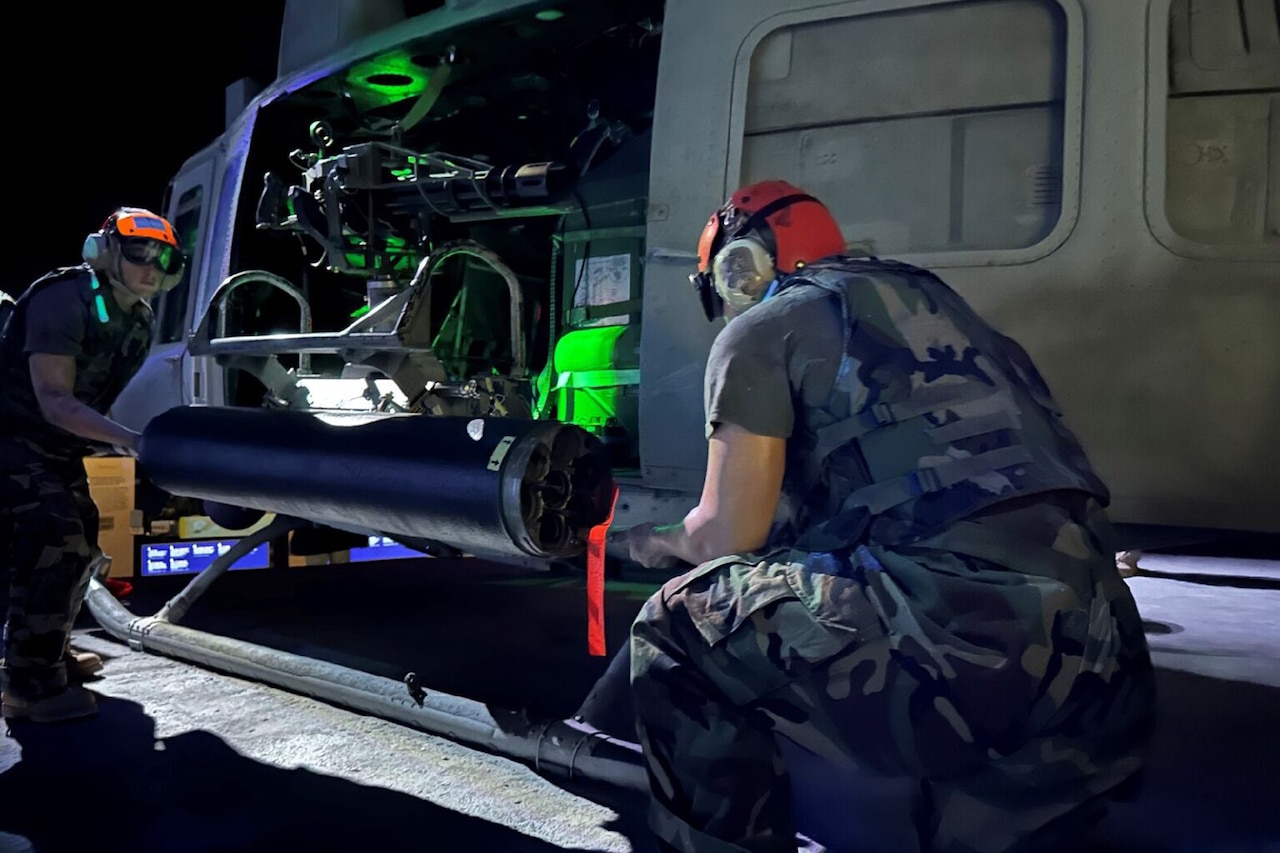 Mannequin's dressed as troops load a helicopter at night in a museum.