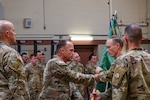 men in U.S. Army uniforms in formation, watching a change of command ceremony which includes passing a guidon flag