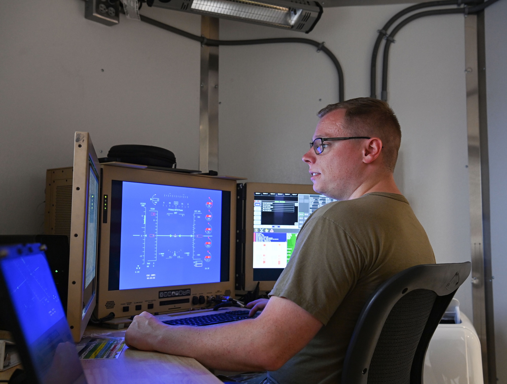 An airman sits in front of a computer with a blue screen.