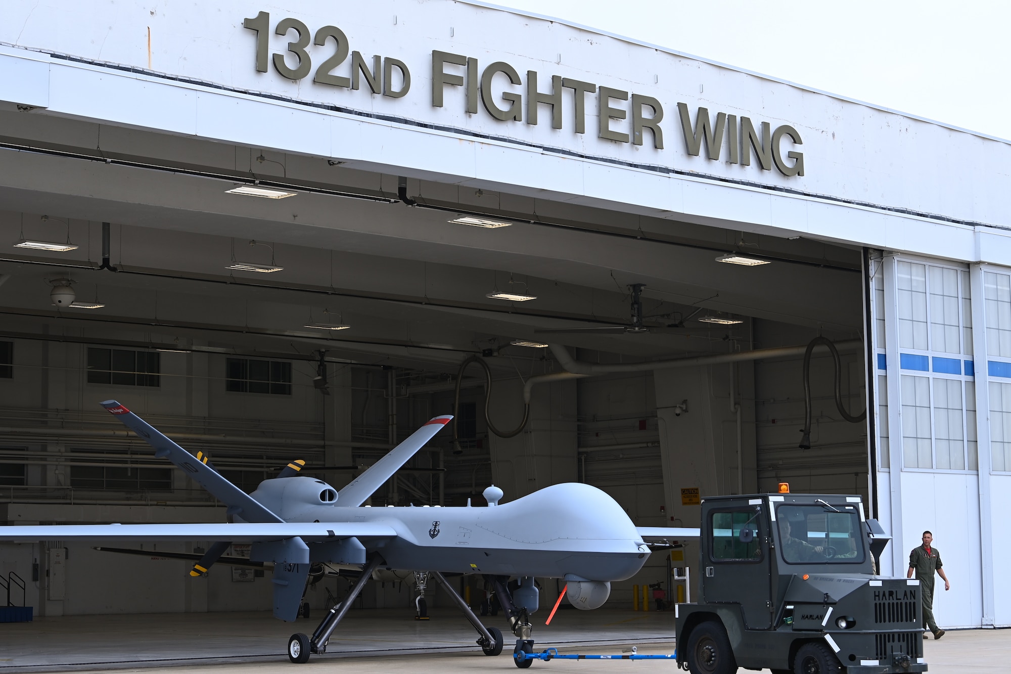 A grey aircraft is wheeled out of a hangar